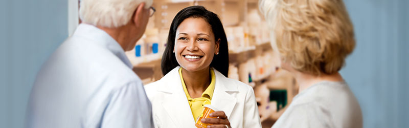 Pharmacist holding pill bottle and talking to senior couple